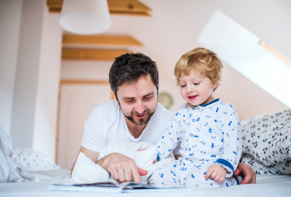 Mature father with toddler boy in bedroom at home, reading stories at bedtime. Paternity leave.