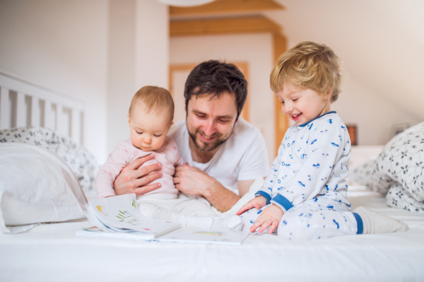 Handsome father with toddler children in bedroom at home, reading stories at bedtime. Paternity leave.