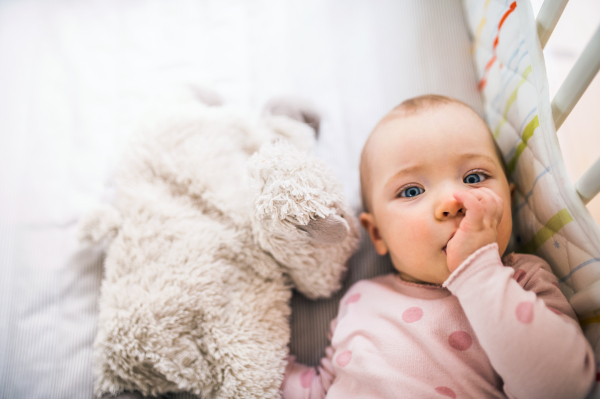 A happy toddler girl lying in a cot in the bedroom at home, a finger in her mouth. Close up. Copy space.