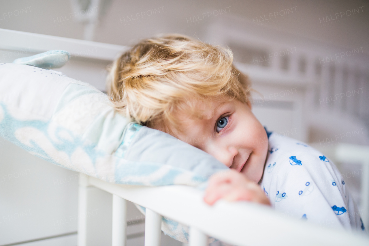 A happy toddler boy standing in a cot in the bedroom at home. Close up.