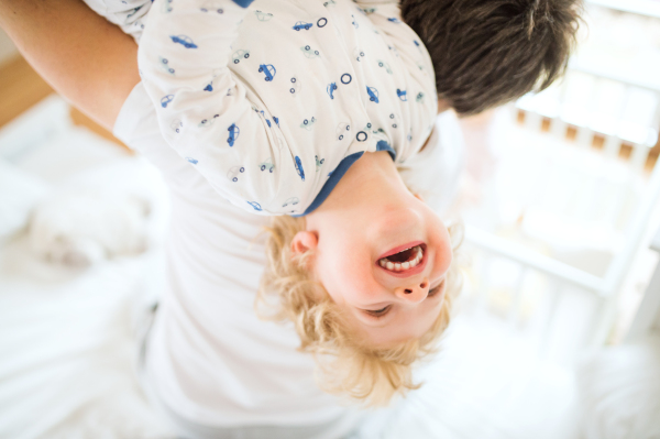 Unrecognizable father holding a happy toddler boy upside down. Paternity leave.