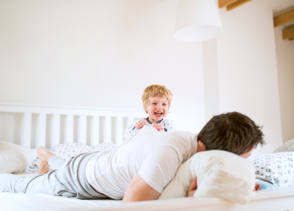 Mature father with a toddler boy having fun in bedroom at home at bedtime. Paternity leave.