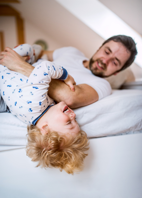 Mature father with a toddler boy having fun in bedroom at home at bedtime. Paternity leave.