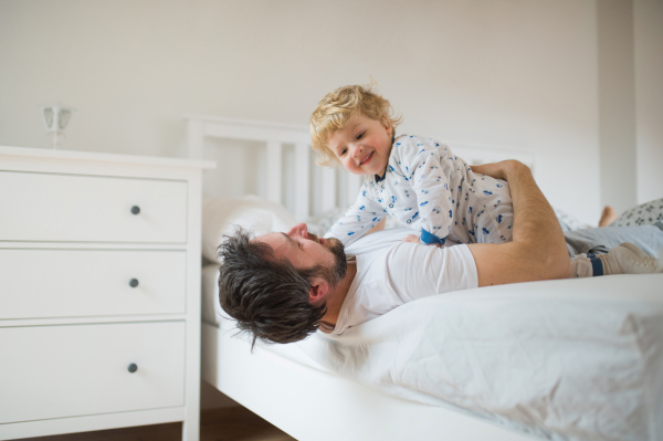 Mature father with a toddler boy having fun in bedroom at home at bedtime. Paternity leave.