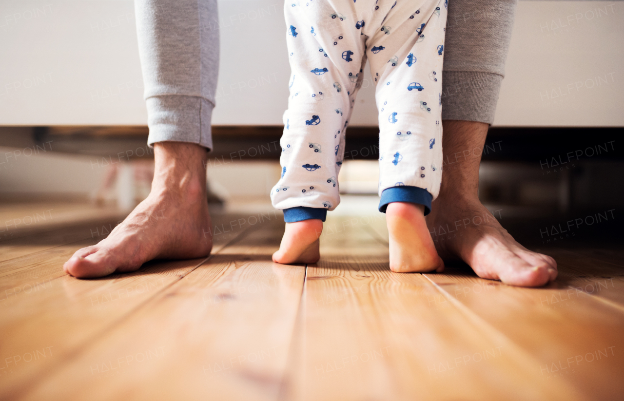 Legs of unrecognizable father and a toddler boy standing on the floor in bedroom at home. Paternity leave. Copy space.