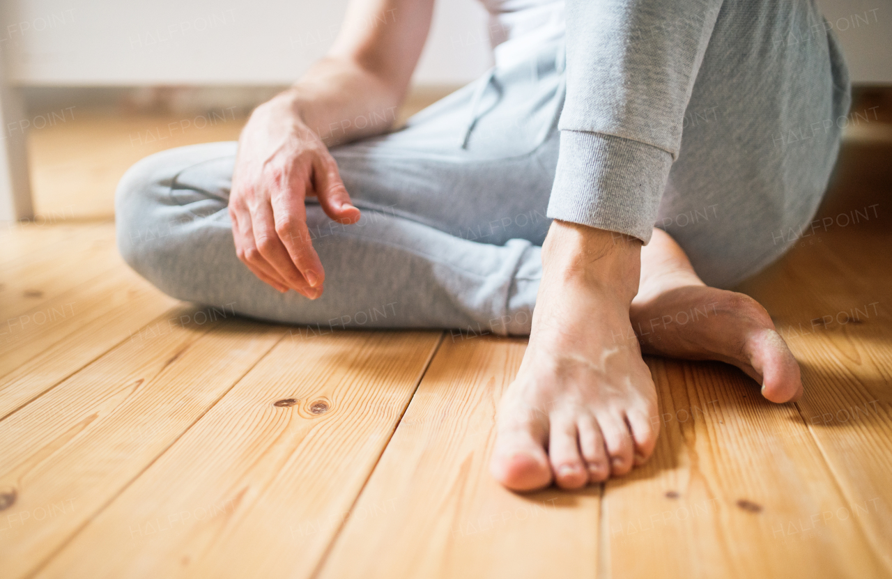 Unrecognizable barefoot man sitting on the floor in bedroom at home.