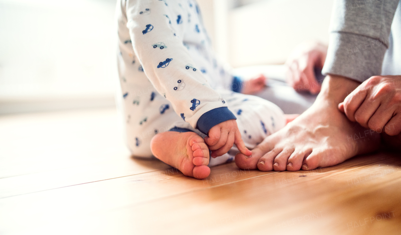 Unrecognizable father with a toddler boy sitting on the floor in bedroom at home at bedtime. Paternity leave.