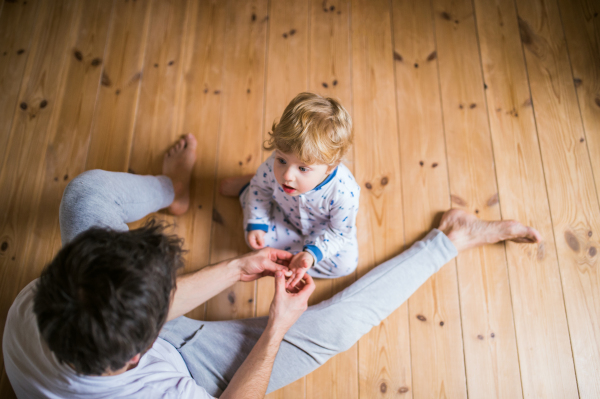 Unrecognizable father with a toddler boy sitting on the floor in bedroom at home at bedtime. Paternity leave. Top view.