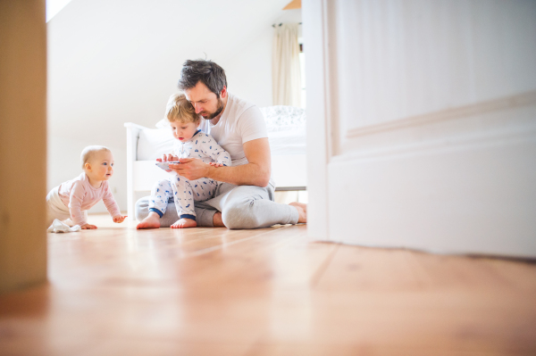 Father and toddler children with smartphone sitting on the floor at home at bedtime. Paternity leave.