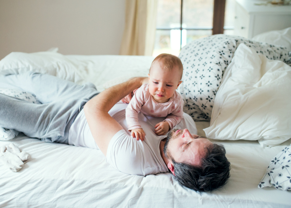 Father with an unhappy toddler girl on bed at home at bedtime. Paternity leave.