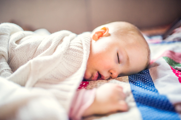 A cute toddler girl sleeping on a bed at home.