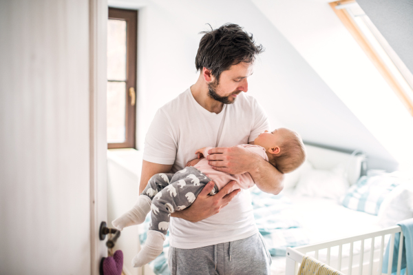 Mature father carrying a sleeping toddler girl in bedroom at home. Paternity leave.