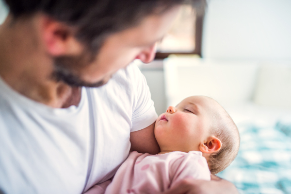 Unrecognizable father holding a sleeping toddler girl at home. Paternity leave.