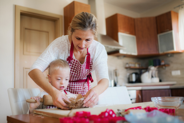 A handicapped down syndrome boy and his mother with checked aprons indoors baking in a kitchen.