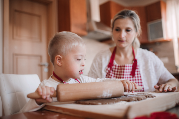 A handicapped down syndrome child and his mother with checked aprons indoors baking in a kitchen.