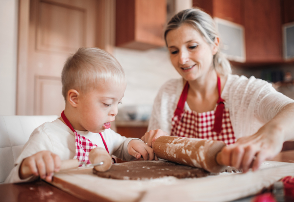 A handicapped down syndrome child and his mother with checked aprons indoors baking in a kitchen.