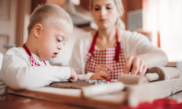 A handicapped down syndrome boy and his mother with checked aprons indoors baking in a kitchen.