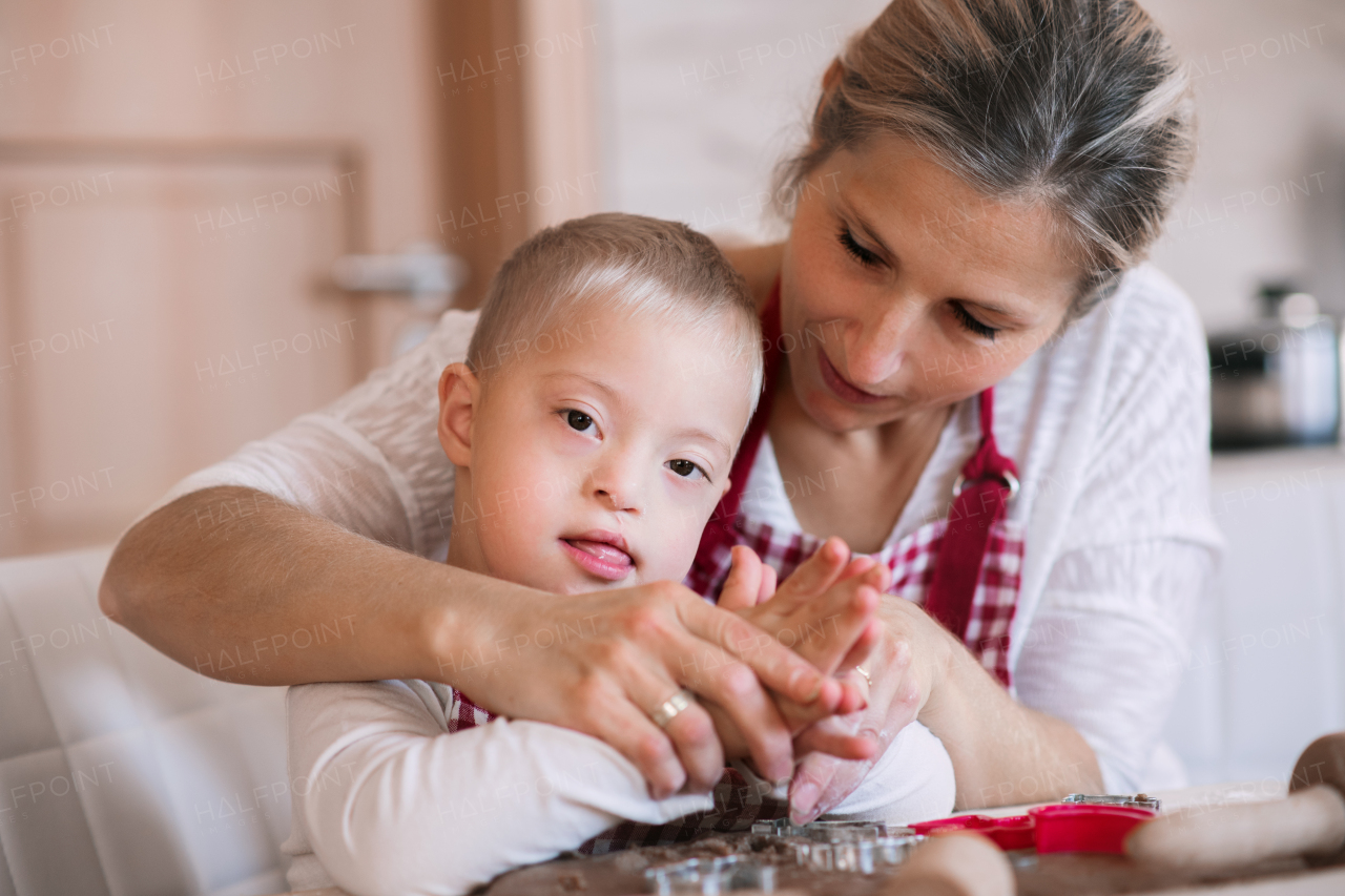 A handicapped down syndrome boy and his mother with checked aprons indoors baking in a kitchen.