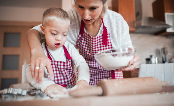 A happy handicapped down syndrome child and his mother indoors baking in a kitchen.