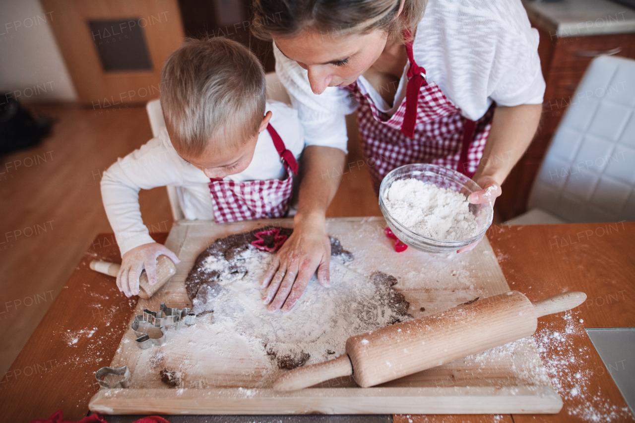 A handicapped down syndrome child and his mother with checked aprons indoors baking in a kitchen. A top view.