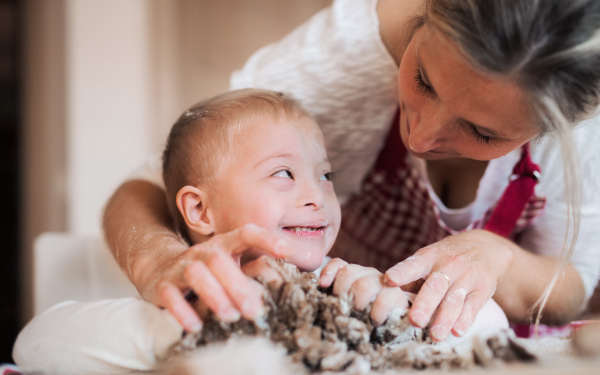 A handicapped down syndrome boy and his mother with aprons indoors baking in a kitchen.