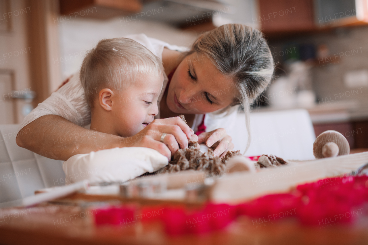 A happy handicapped down syndrome child and his mother indoors baking in a kitchen.