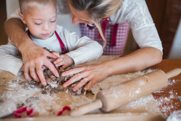 A happy handicapped down syndrome child and his mother indoors baking in a kitchen.