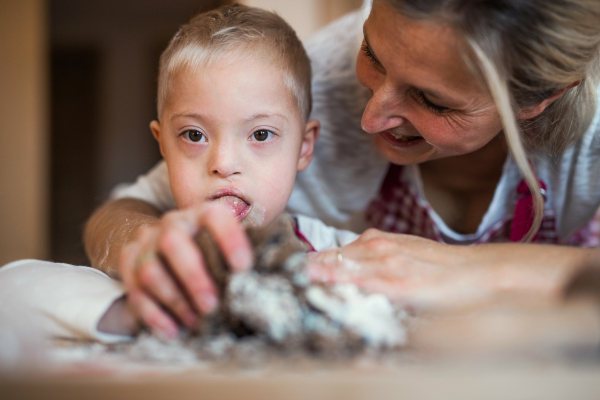 A happy handicapped down syndrome child and his mother indoors baking in a kitchen.