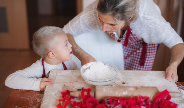 A handicapped down syndrome child and his mother with checked aprons indoors baking in a kitchen.