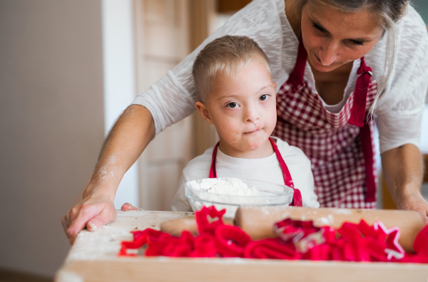 A happy handicapped down syndrome child and his mother indoors baking in a kitchen.