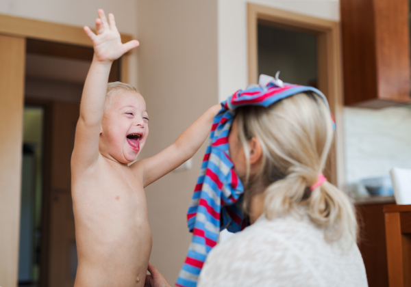 A laughing handicapped down syndrome boy playing with his unrecognizable mother indoors, having fun.