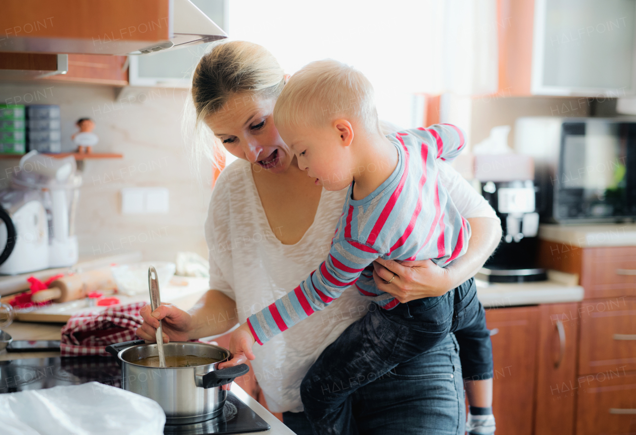 A handicapped down syndrome boy cooking soup with his mother indoors. Dinner or lunch time.