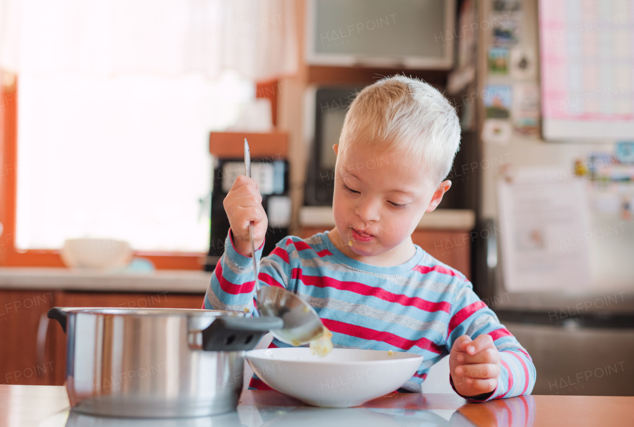 A handicapped down syndrome child pouring soup into a plate indoors before lunch.