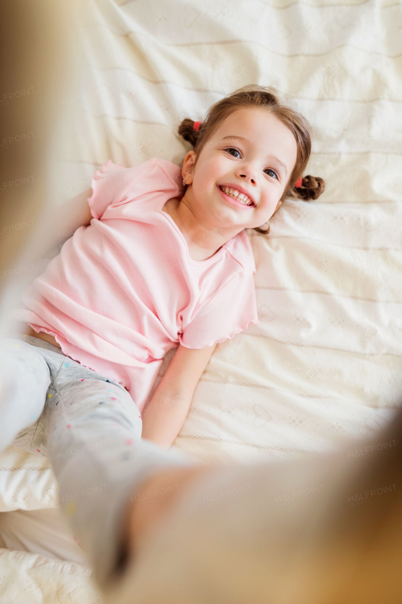 Cute little girl in pink t-shirt with two braids in bedroom jumping on a bed