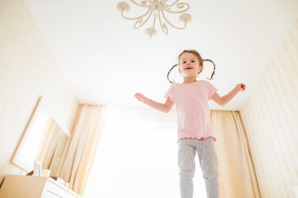 Cute little girl in pink t-shirt with two braids in bedroom jumping on a bed