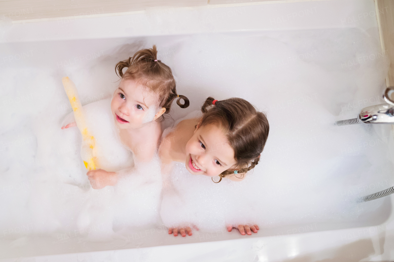 Two cute little girls having bath with bubbles in bathtub