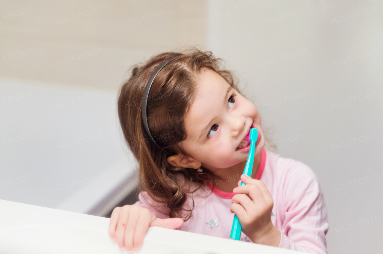 Cute little girl in pink pyjamas in bathroom brushing her teeth