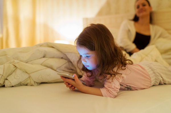 Cute little girl with smartphone lying in a bed, bedtime