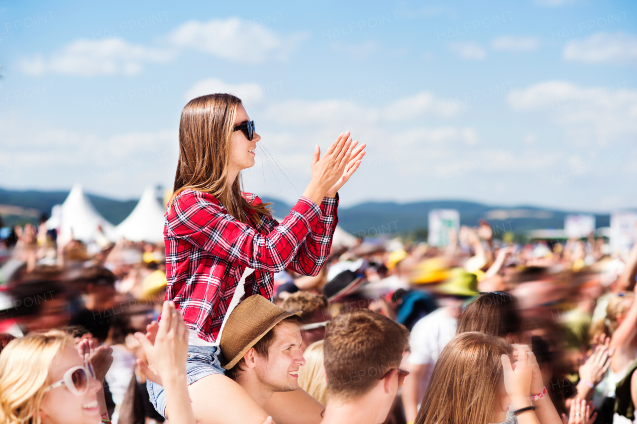 Teenage couple at summer music festival under the stage in a crowd enjoying themselves. Handsome man giving beautiful young woman piggyback.