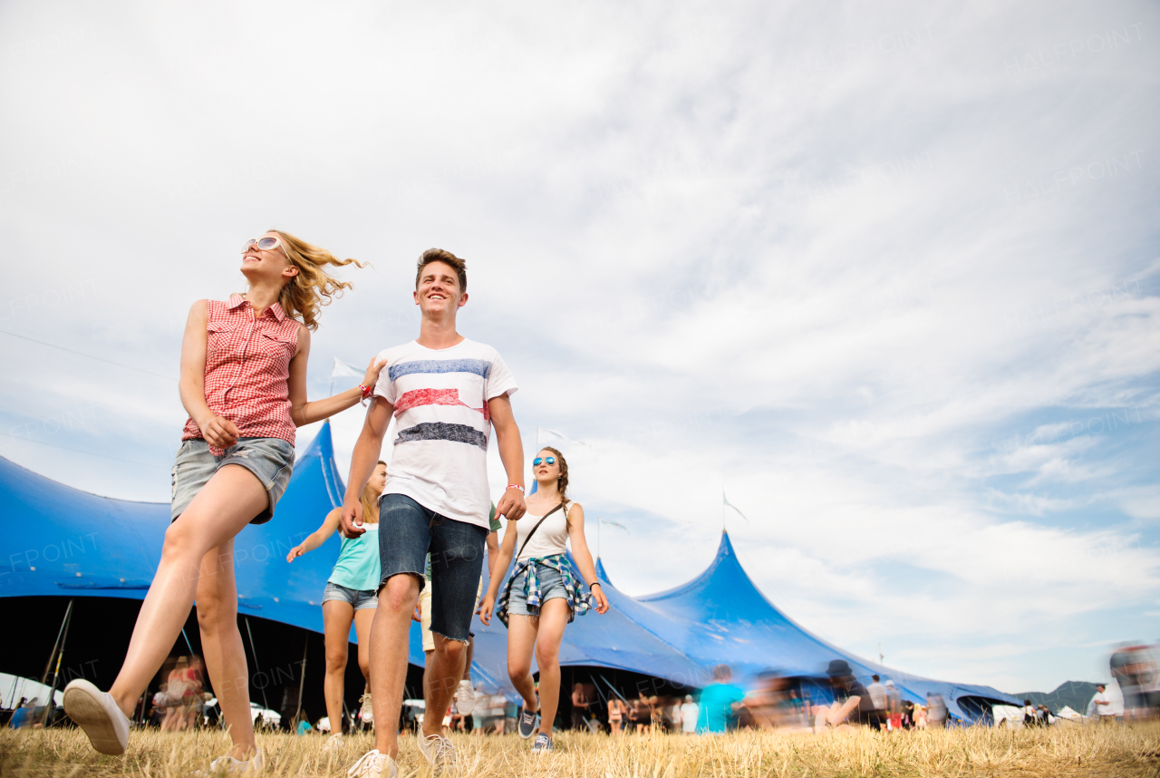 Group of teenage boys and girls at summer music festival walking in front of big blue tent, sunny day