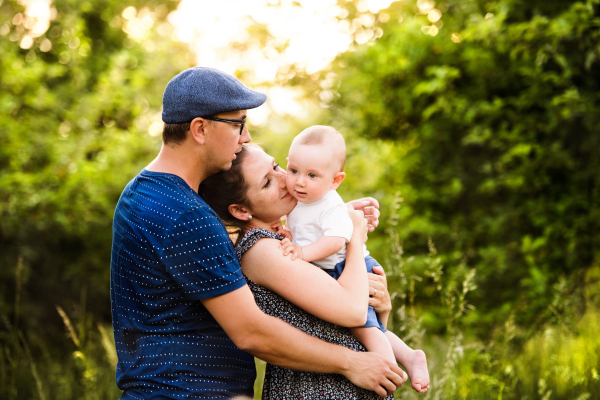 Happy young family with little son spending time together outside in green summer nature