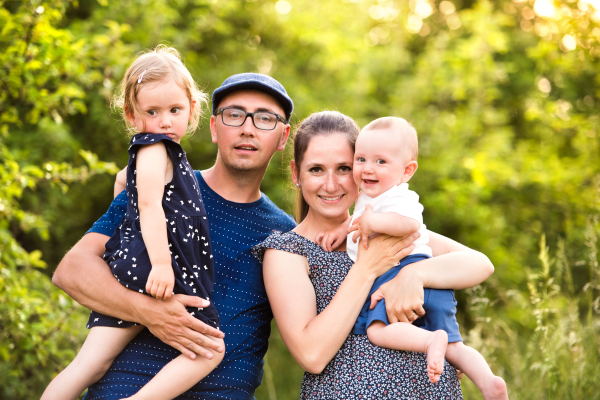 Happy young family with little children spending time together outside in green summer nature