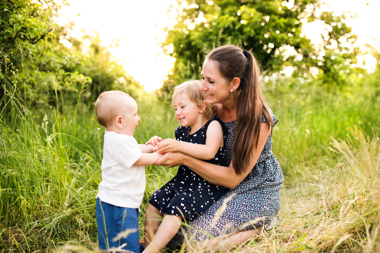 Beautiful young mother with little children spending time together outside in green summer nature.