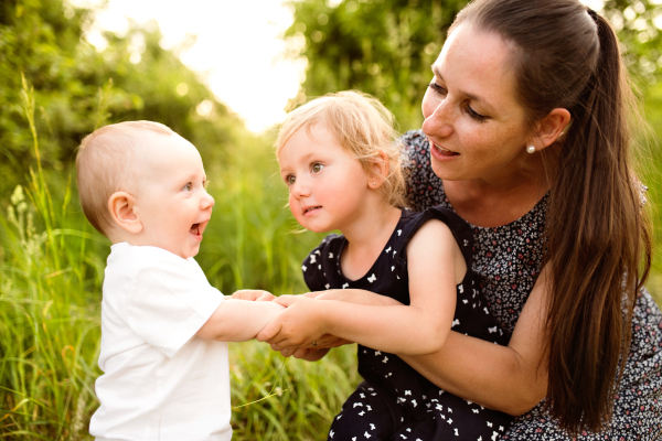 Beautiful young mother with little children spending time together outside in green summer nature