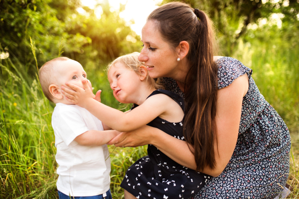 Beautiful young mother with little children spending time together outside in green summer nature.