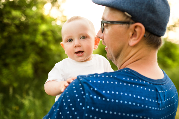 Young father in green summer nature holding his cute baby son in the arms.