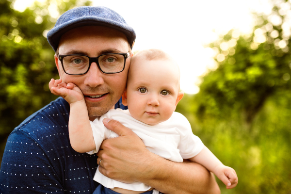 Young father in green summer nature holding his cute baby son in the arms.