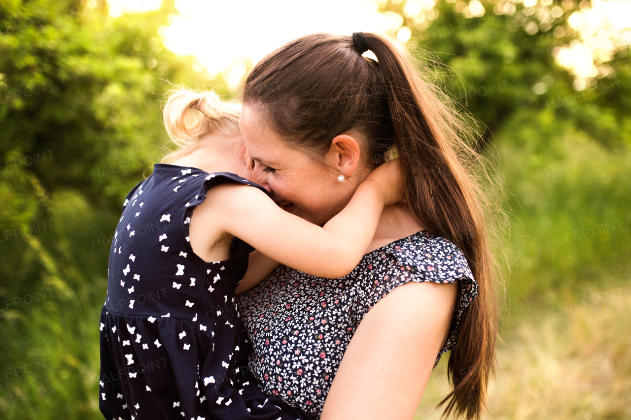 Beautiful young mother in green sunny summer nature holding her cute little daughter in the arms.