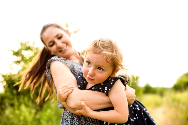 Beautiful mother spinning her cute little daughter. Sunny summer day in nature.