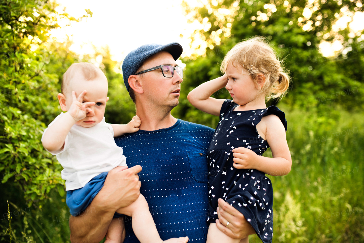 Happy young father with little children spending time together outside in green summer nature